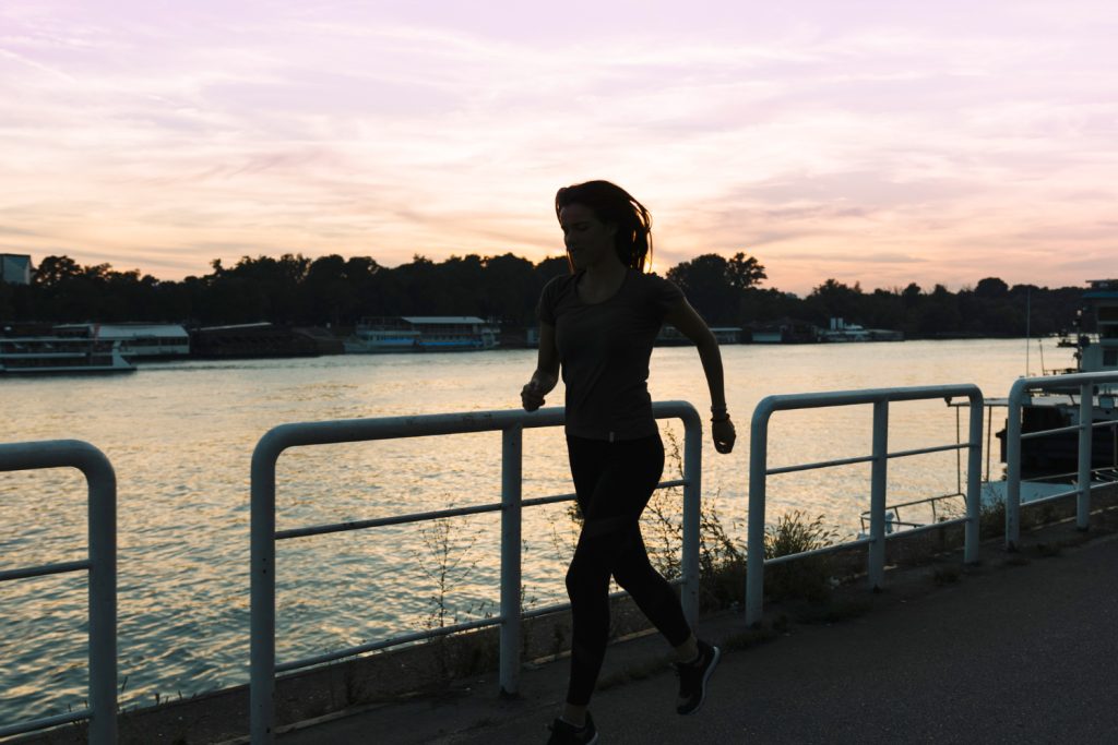 Silhouette of a woman running on street near river